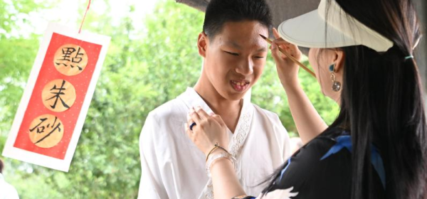 A volunteer dots cinnabar on a child's forehead on the Dragon Boat Festival at Huiai Farm in Yangliuqing Town, Xiqing District, north China's Tianjin