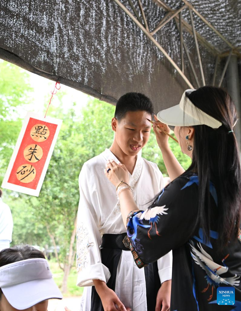 A volunteer dots cinnabar on a child's forehead on the Dragon Boat Festival at Huiai Farm in Yangliuqing Town, Xiqing District, north China's Tianjin