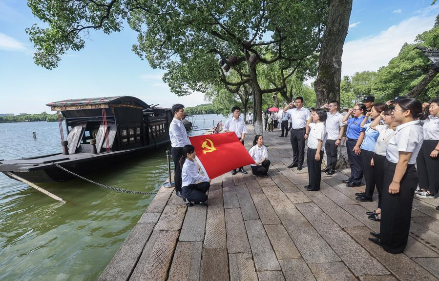Members of the Communist Party of China (CPC) review the Party admission oath beside the replica of a boat, now referred to as the Red Boat, on which CPC founders concluded their meeting in 1921, on Nanhu Lake in Jiaxing, east China's Zhejiang Province, June 30, 2025. (Xinhua/Xu Yu)