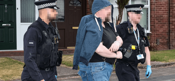 A man is led in handcuffs after a raid at a house in Bolton