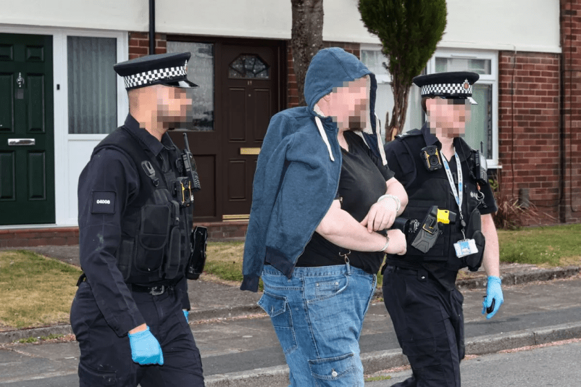 A man is led in handcuffs after a raid at a house in Bolton