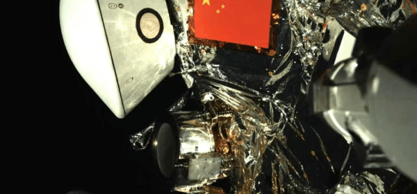 This image released by the China National Space Administration (CNSA) on Oct. 1, 2025 shows a view of the Tianwen-2 probe alongside Earth, captured by the probe during its deep-space journey. The newly released image, acquired by a monitoring camera mounted on the probe's robotic arm, showcases China's five-starred red flag and the white return capsule against the backdrop of a distant, blue Earth. (CNSA/Handout via Xinhua)