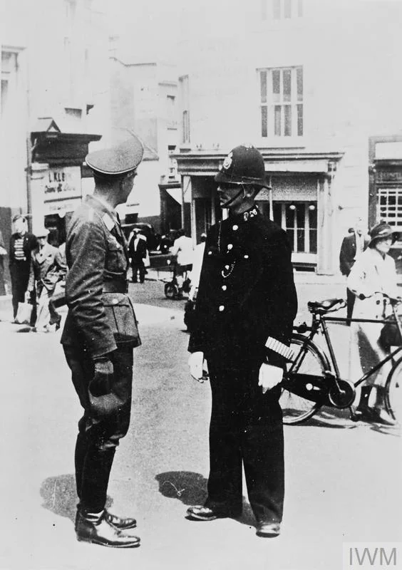 "A German air force officer talking to a British policeman in a Jersey street shortly after the occupation of the island (1940)". Photographs of the iconic British bobby cooperating with Reich authorities had immense propaganda value for the Germans