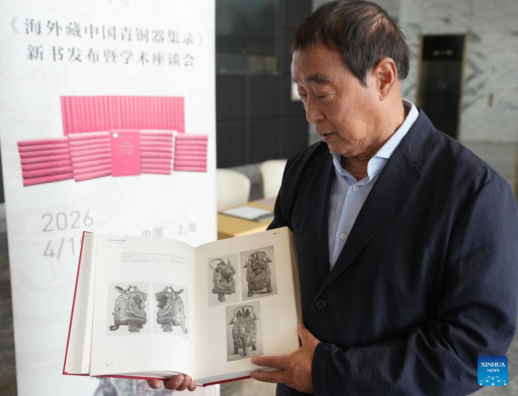 Professor Zhu Fenghan, the lead editor of a sixty-volume compendium documenting more than 23,000 ancient Chinese bronze artifacts lost abroad, displays detailed contents in one of the books during a press conference for the books' release in east China's Shanghai, April 19, 2026. (Xinhua/Liu Ying)