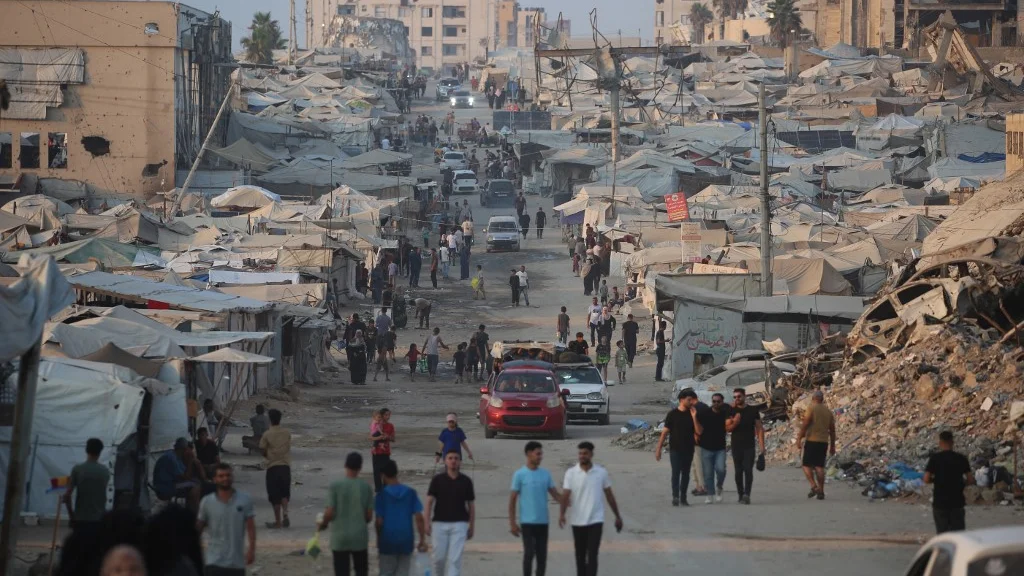 Displaced Palestinians walk past tents and destroyed buildings near the beachfront in Gaza City on 14 August 2026 (AFP)