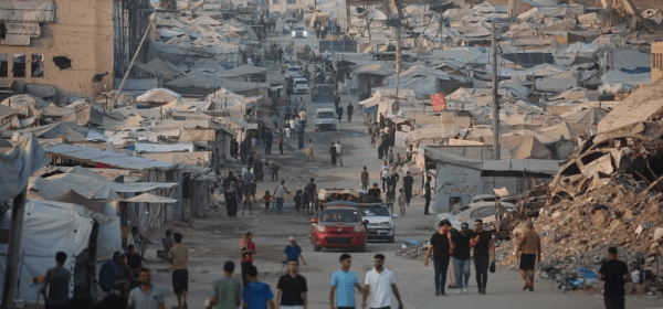 Displaced Palestinians walk past tents and destroyed buildings near the beachfront in Gaza City on 14 August 2026 (AFP)